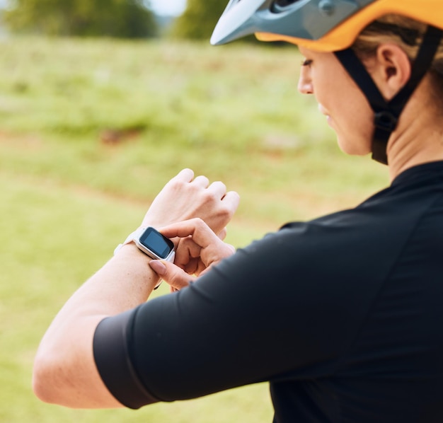 Frequenza cardiaca smartwatch e ciclista donna che controllano il polso all'aperto per il fitness in bici e in bicicletta App per il benessere degli esercizi e atleta femminile che fa un controllo del tempo per la corsa ciclistica in natura sull'erba