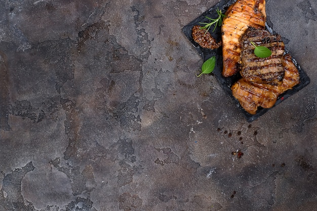 Freschi tre tipi di bistecca alla griglia (pollo, maiale, manzo) sul piatto di ardesia con le erbe