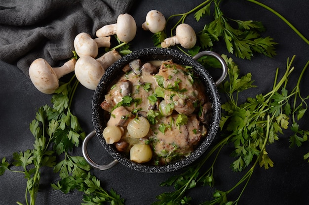 Fricassea - Cucina francese. Pollo in umido in salsa cremosa con funghi in casseruola su un tavolo nero