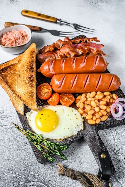 Friggere la colazione all'inglese con uova fritte, salsicce, pancetta, fagioli e toast su un tagliere di legno. vista dall'alto.