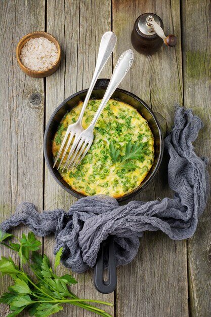 Fritatta con patate, piselli ed erbe aromatiche in una padella di ferro su una vecchia superficie di legno