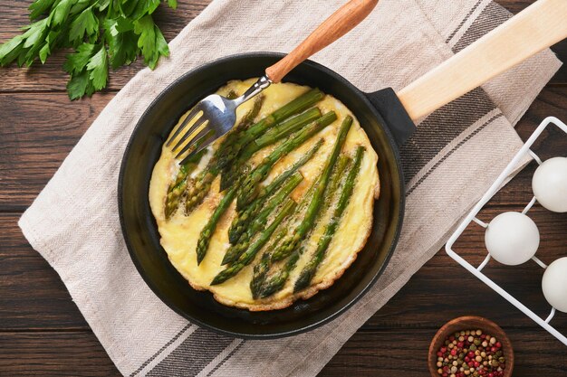 Frittata con asparagi Frittata o strapazzate con asparagi in padella con prezzemolo e pepe su un vecchio sfondo di tavolo in legno Utile concetto di colazione Vista dall'alto