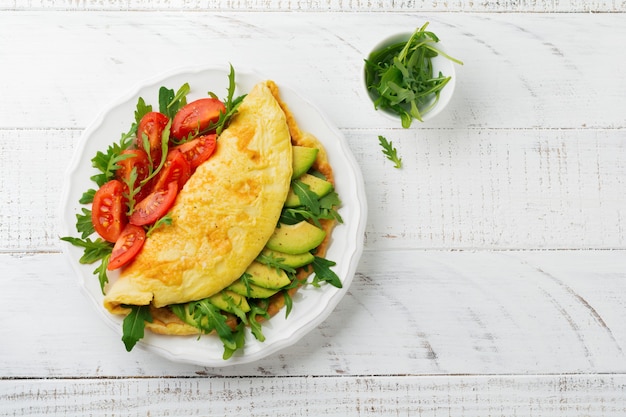 Frittata con avocado, pomodori e rucola sul piatto in ceramica bianca