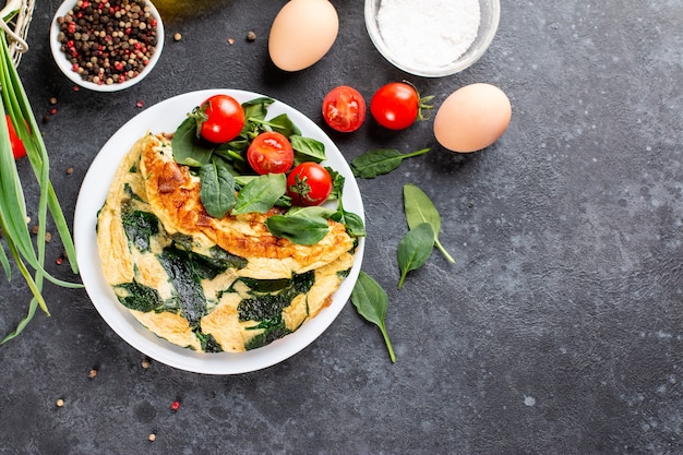 Frittata con foglie di spinaci. Frittata alla piastra, uova strapazzate su uno sfondo scuro di ardesia, pietra o cemento. Vista dall'alto. Copia spazio.