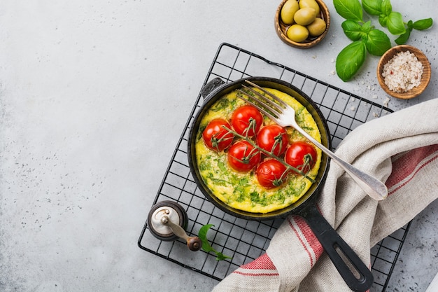 Frittata con rucola, patate e pomodorini in padella di ferro su un vecchio tavolo in pietra. Vista dall'alto.