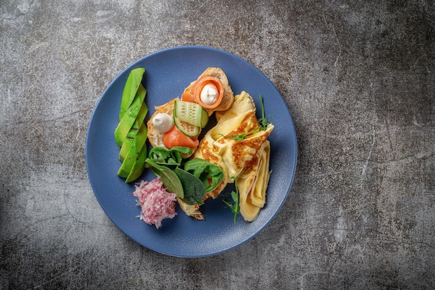 Frittata con salmone, erbe fresche e pomodori in un piatto blu con spezie contro un tavolo di pietra grigia