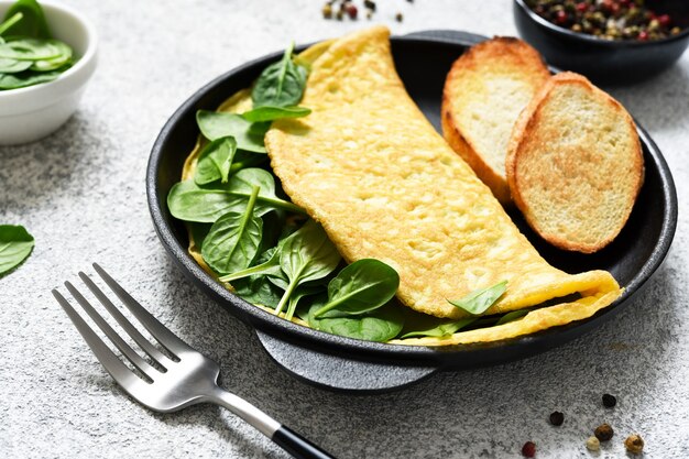 Frittata con spinaci per colazione in padella di ghisa su fondo in cemento.