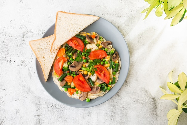 Frittata con vagetable, pomodori, funghi, fagiolini, pease, mais, pane tostato a lievitazione naturale isolato su sfondo di marmo bianco. Cibo fatto in casa. Gustosa colazione Messa a fuoco selettiva. Foto di Hotizontal.