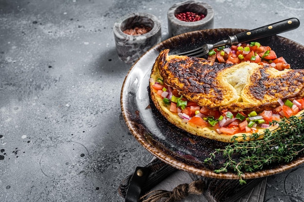 Frittata di uova ripiene con pomodoro, cipolla ed erbe aromatiche su un piatto. Sfondo grigio. Vista dall'alto. Copia spazio.