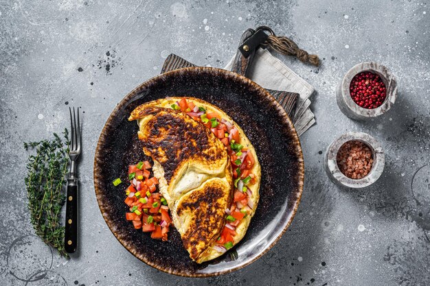 Frittata di uova ripiene con pomodoro, cipolla ed erbe aromatiche su un piatto. Sfondo grigio. Vista dall'alto.