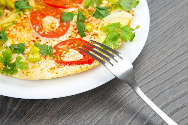 Frittata fritta cotta con erbe e verdure in un piatto bianco su un tavolo di legno