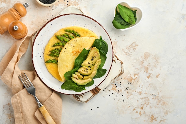 frittata o frittata farcita con asparagi, avocado e foglie di spinaci per colazione su piatto bianco white