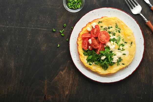 Frittata rustica o frittate con cipolle verdi formaggio mozzarella rucola verde e pomodori su legno vecchio sfondo scuro Cibo sano concetto Colazione Copia spazio Vista dall'alto Mock up