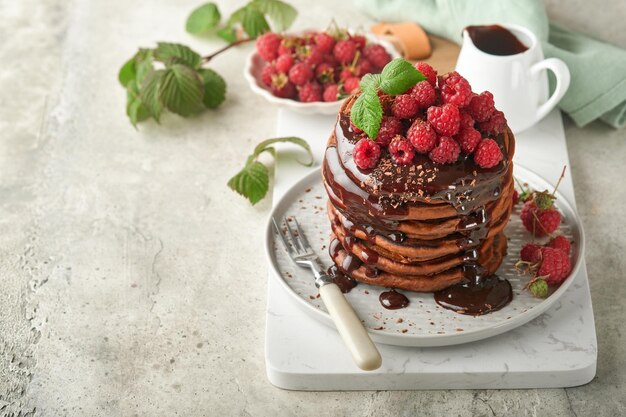 Frittelle al cioccolato Frittelle con lampone fresco con glassa al cioccolato o condimenti in una ciotola grigia su sfondo grigio chiaro del tavolo Frittelle americane classiche fatte in casa Pagina per il concetto di rivista