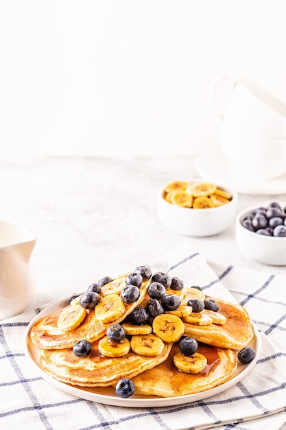 Frittelle con banana, mirtilli sul piatto bianco, fuoco selettivo.