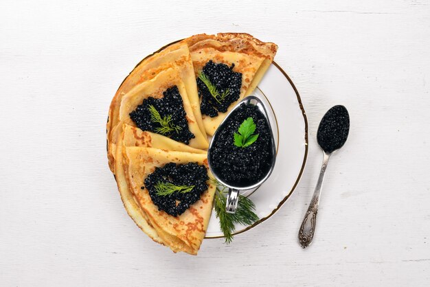 Frittelle con caviale nero su un piatto Su uno sfondo di legno Vista dall'alto Spazio libero per il testo