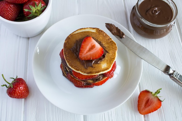 Frittelle con crema di fragole e cioccolato nel piatto su fondo di legno bianco