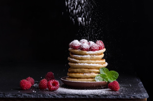 Frittelle con lamponi e frutti di bosco intorno su sfondo nero