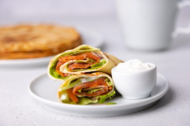 Frittelle con panna acida di trota salmonata e verdure Blinchiki sottili non dolci ripieni di pesce rosso Piatto tradizionale russo e ucraino Festa di Maslenitsa Messa a fuoco selettiva Primo piano