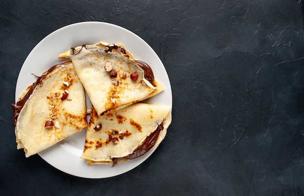 Frittelle con pasta di cioccolato e nocciole, su un piatto bianco su uno sfondo di cemento, ardesia con copia spazio per il testo