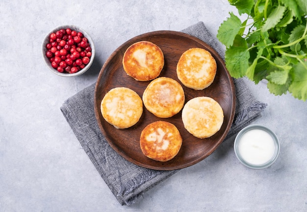 Frittelle con ricotta con mirtilli freschi e panna acida su un piatto di legno su sfondo blu Il concetto di una sana e deliziosa colazione mattutina