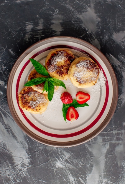 frittelle di cagliata con fragole e menta e zucchero a velo in un piatto bianco.