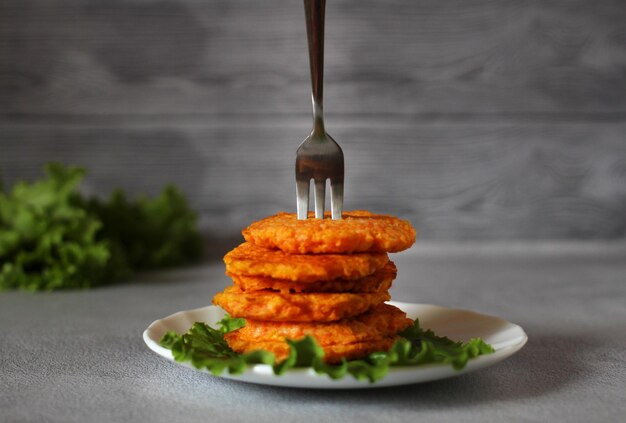 Frittelle di carote dietetiche naturali su un piatto con foglie di lattuga e una forchetta su sfondo grigio