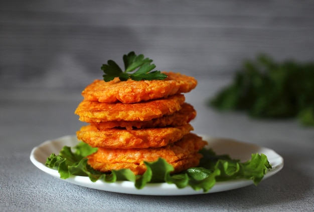 Frittelle di carote dietetiche naturali su un piatto con foglie di lattuga e una forchetta su sfondo grigio