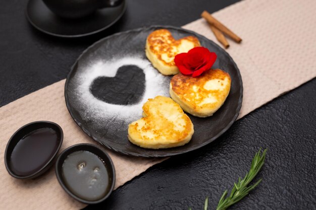 Frittelle di cheesecake alla cagliata a forma di cuore con miele e marmellata su un piatto nero