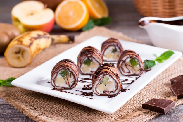 Frittelle di cioccolato sottili arrotolate su un piatto su uno sfondo di legno