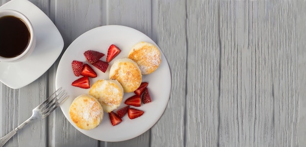 Frittelle di formaggio con fragola e tazza di caffè sullo sfondo di legno grigio Vista dall'altoCopia spazio