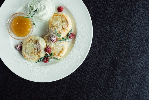 Frittelle di formaggio con lamponi e miele su un piatto bianco su un tavolo di legno