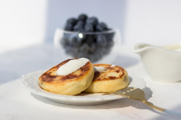 Frittelle di formaggio con mirtilli su un tavolo bianco Mattina raggi del sole Buongiorno cartolina