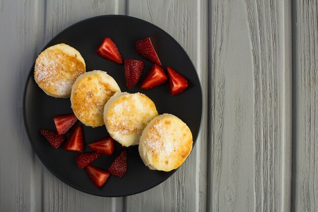 Frittelle di formaggio e fragole sul piatto scuro su fondo di legno grigio.Vista dall'alto.spazio copia.