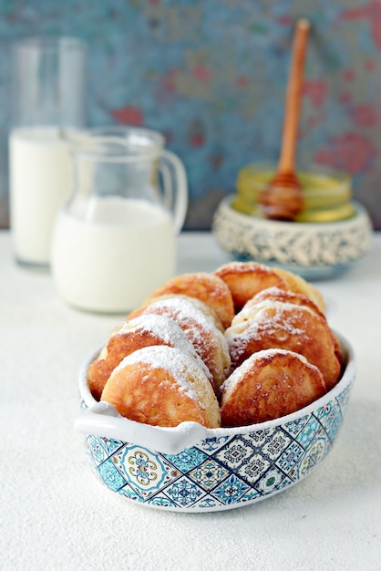 Frittelle di lievito in zucchero a velo con latte e miele su una superficie leggera.