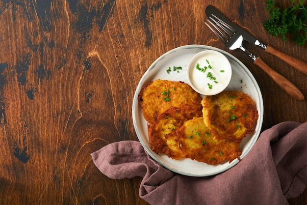 Frittelle di patate frittelle di patate fatte in casa o latkes con panna e cipolle verdi in un piatto rustico su un vecchio tavolo in legno su sfondo rustico Stile rustico Cibo sano Vista dall'alto