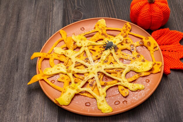 Frittelle di ragnatela con sciroppo di zucchero e polvere per la colazione di Halloween. Con uncinetto all'arancia zucca e foglia