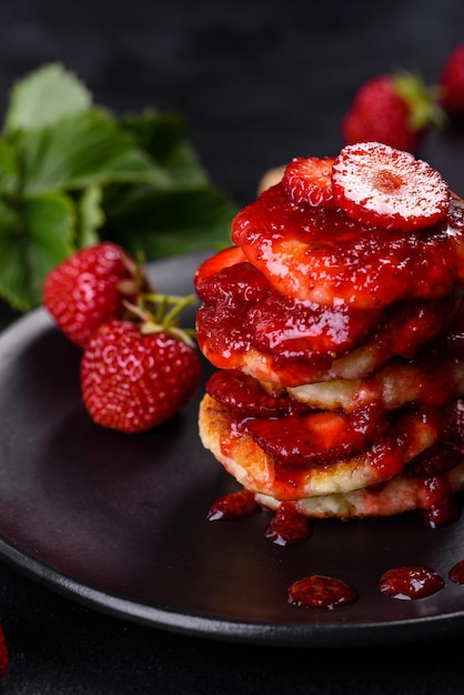 Frittelle di ricotta con fragole a fette e marmellata di fragole su un piatto su uno sfondo di cemento