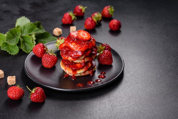 Frittelle di ricotta con fragole a fette e marmellata di fragole su un piatto su uno sfondo di cemento