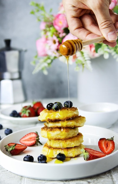 Frittelle di ricotta con fragole fresche, mirtilli e miele a mano. Colazione