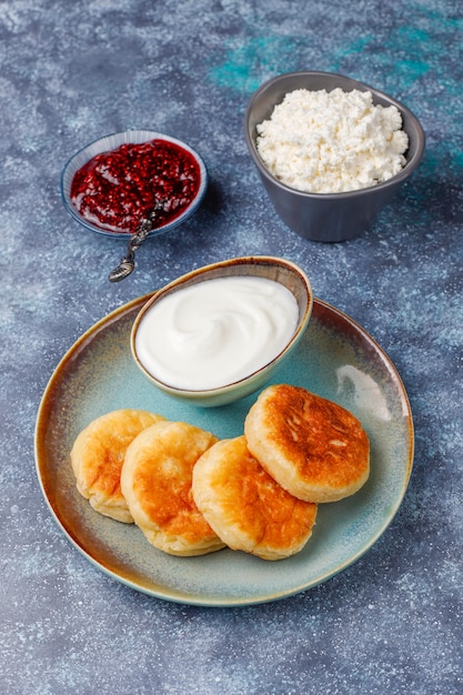 Frittelle di ricotta con marmellata di lamponi. Syrniki russo o sirniki, frittelle di ricotta o pancake con una ciotola di ricotta fresca fatta in casa su grigio scuro