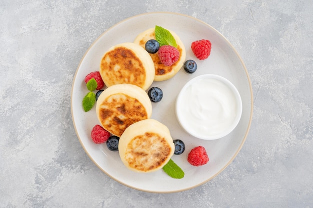 Frittelle di ricotta con panna acida ai frutti di bosco freschi e miele tradizionale syrniki