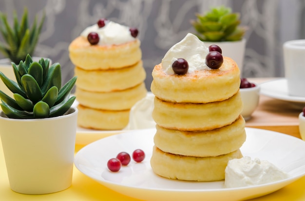 Frittelle di ricotta con panna acida e frutti di bosco su sfondo giallo. Syrniki.