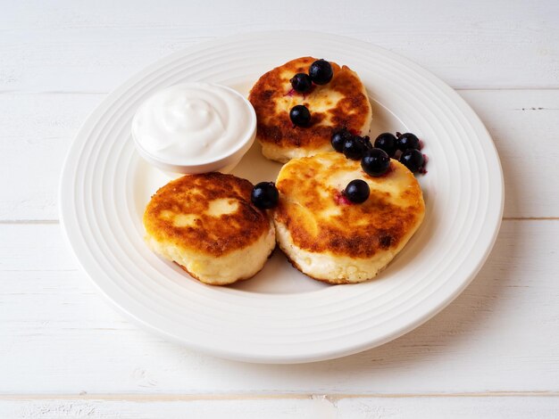 Frittelle di ricotta con panna acida e ribes nero su un piatto di ceramica bianca Concetto di colazione