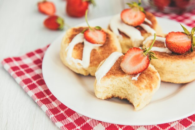 Frittelle di ricotta fatte in casa con panna acida e fragole fresche su fondo di legno bianco.