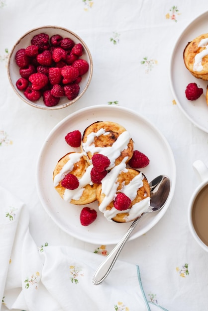 Frittelle di ricotta in piatto bianco Syrniki con lamponi e panna acida