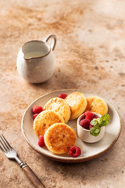 Frittelle di ricotta syrniki con miele guarnito e fresco lampone e foglie di menta su rustico piatto in ceramica su sfondo testurizzato Orientamento verticale