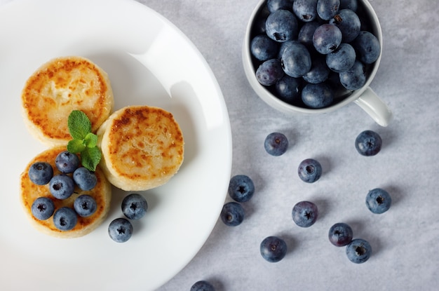 Frittelle di ricotta, syrniki con mirtilli in un piatto bianco.