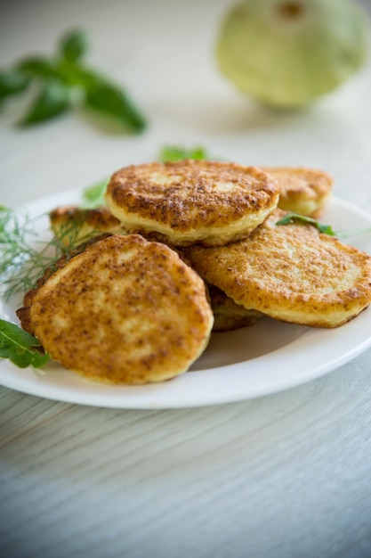 Frittelle di verdure fritte di zucca e zucchine alle erbe su un tavolo di legno chiaro