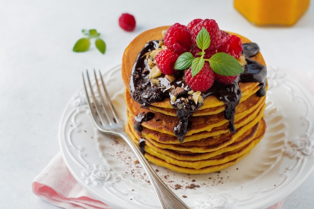 Frittelle di zucca con lamponi freschi, cioccolato e noci su pietra chiara o cemento.